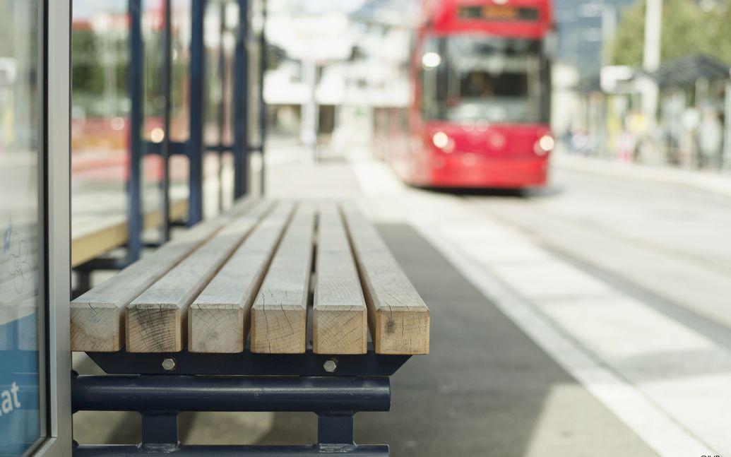 Close-up of a bench at the stop, with tram arriving at stop in background